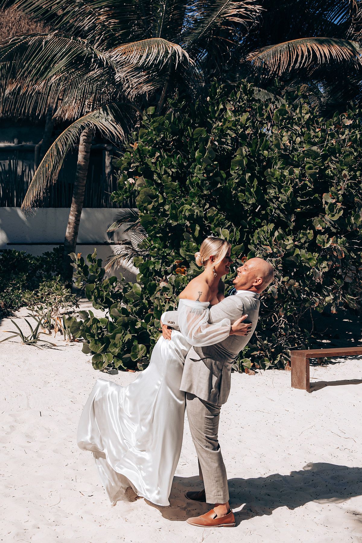 A romantic moment between newlyweds dancing on a sandy beach under palm trees.