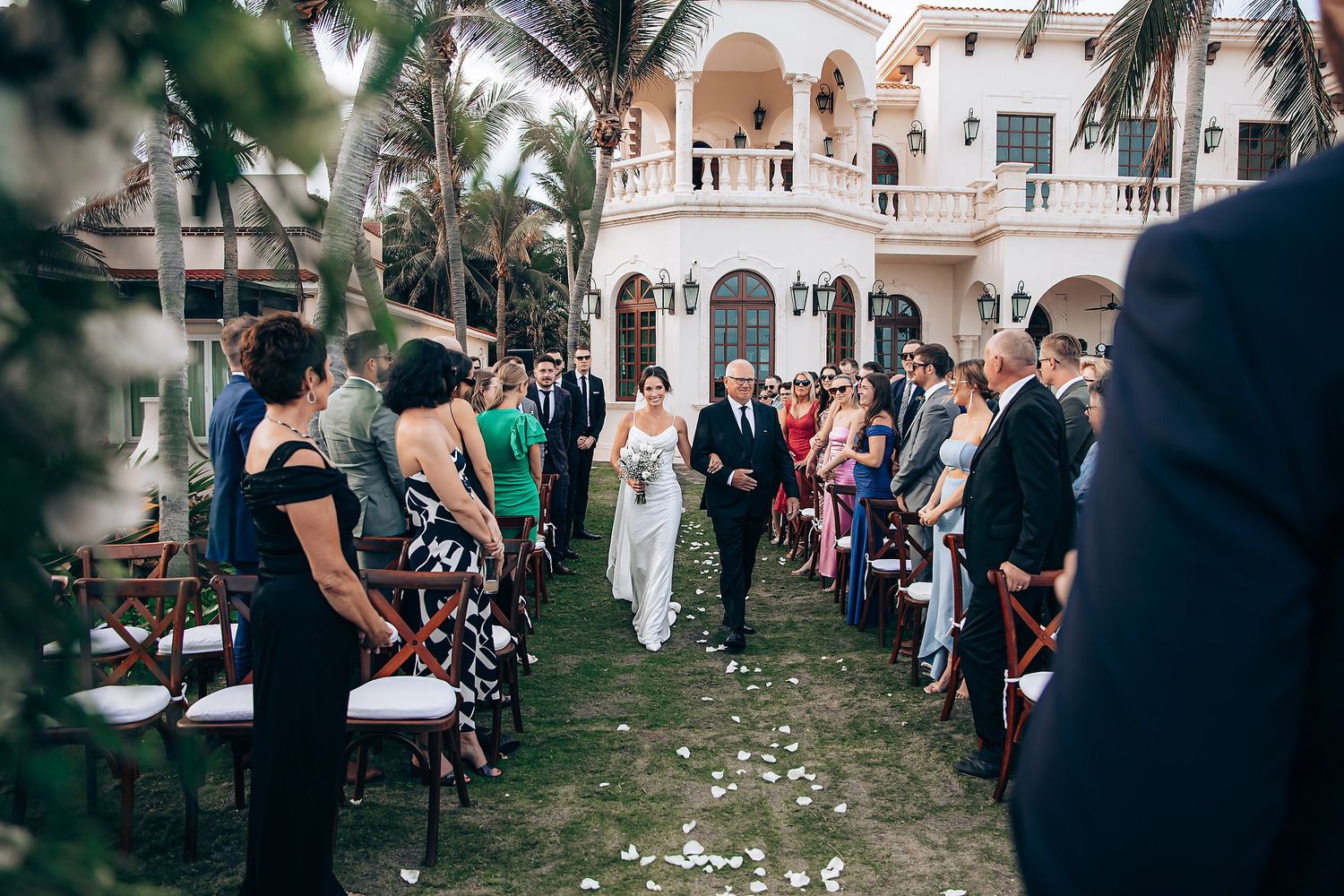 Wedding ceremony processional with guests seated outdoors at an elegant venue.