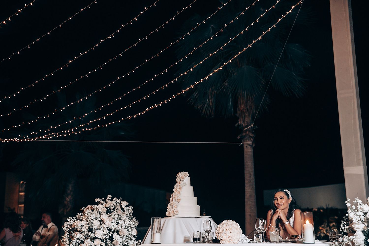 Wedding reception space with hanging lights and tiered white wedding cake.