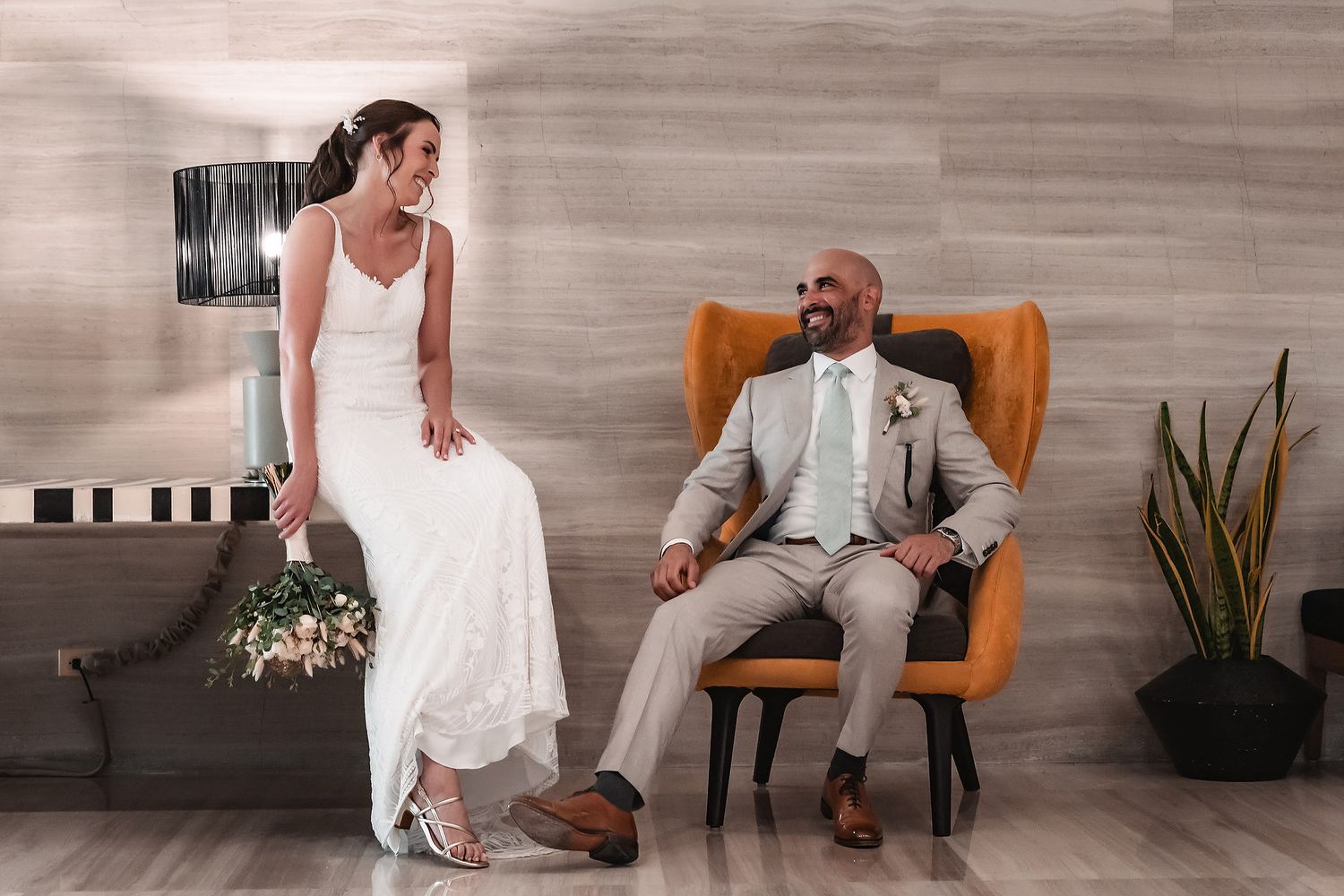 Intimate wedding scene with couple seated in orange and woven chairs against light wood paneling.