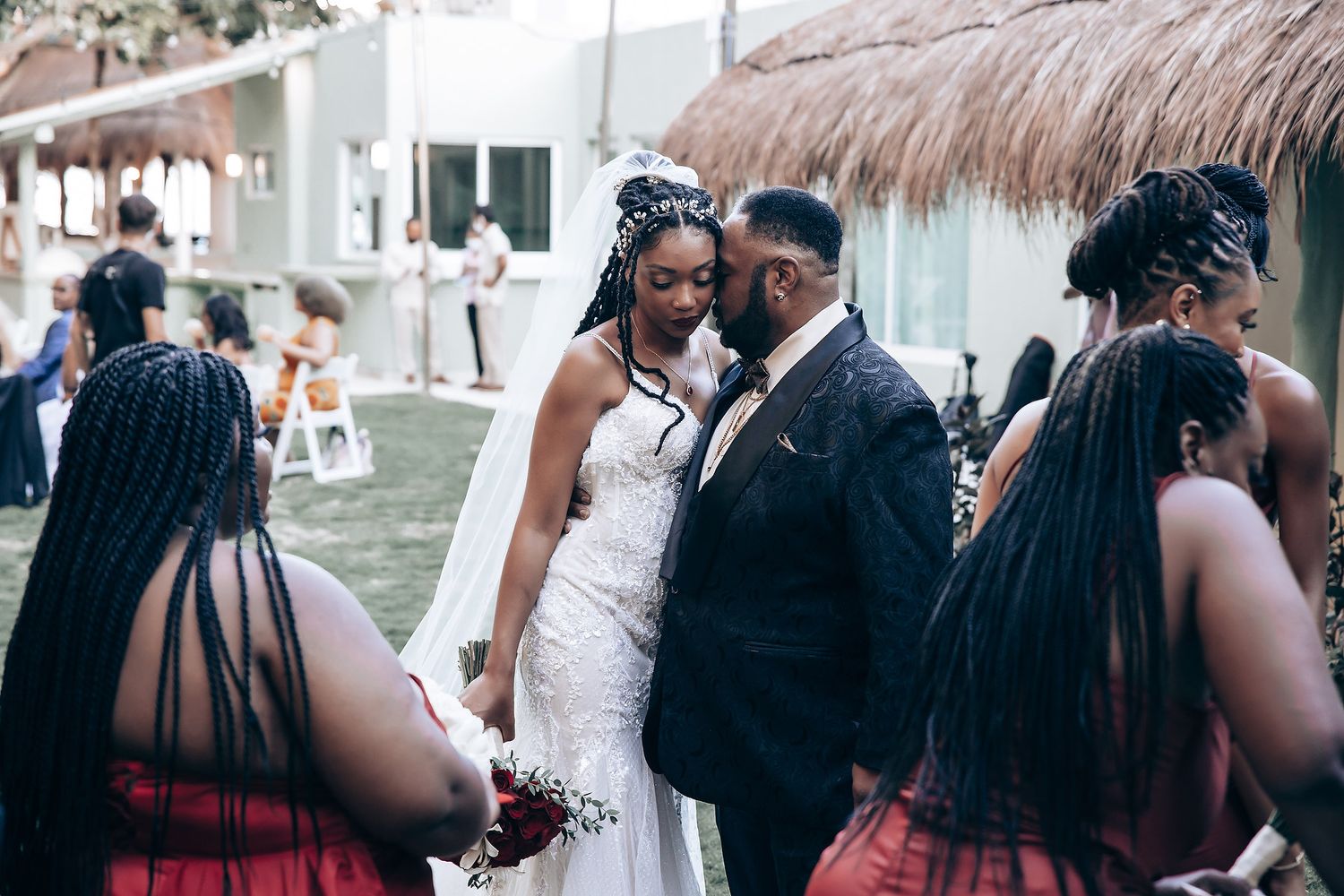 A romantic wedding celebration with a couple in formal attire surrounded by bridesmaids with braided hair at a tropical venue.