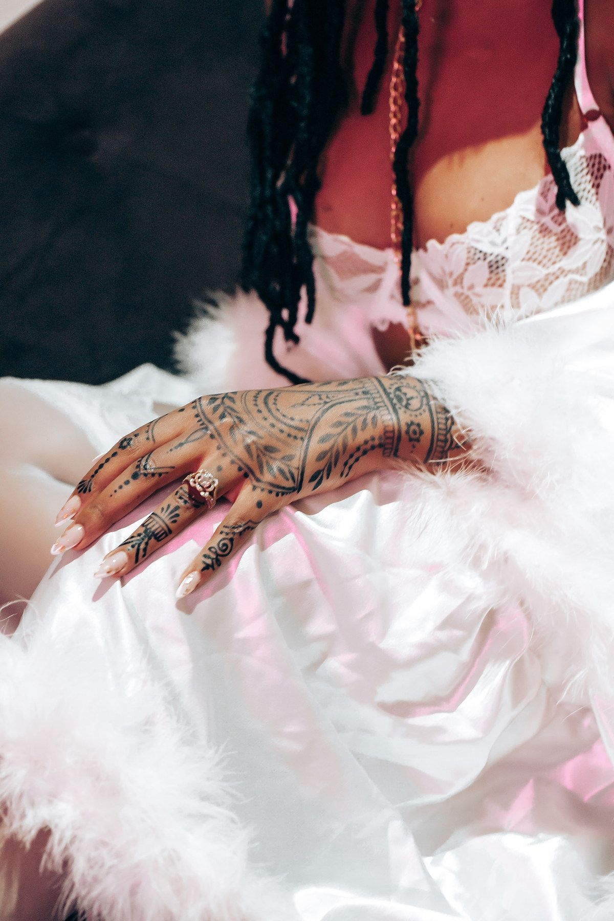 Close-up view of decorative henna designs on hands against white feathery fabric with pink lighting.