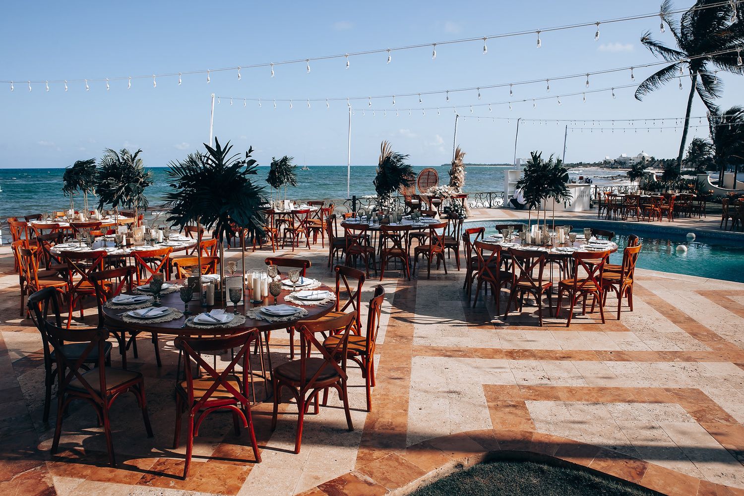 Panoramic view of a beach wedding reception area with wooden furniture and ocean backdrop.