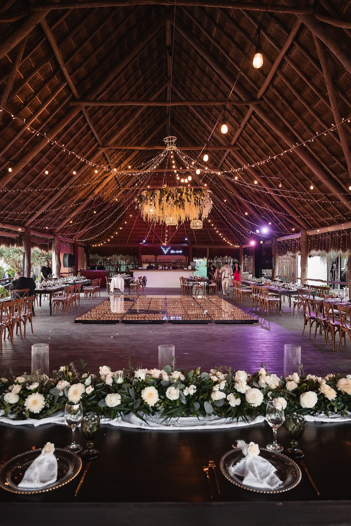 Large thatched-roof reception venue with string lights and floral decorations.