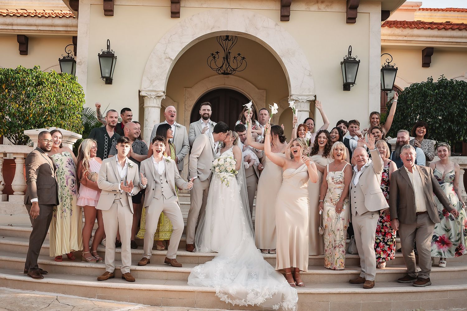 Wedding party poses for photos outside Spanish colonial style building with arched walkways.