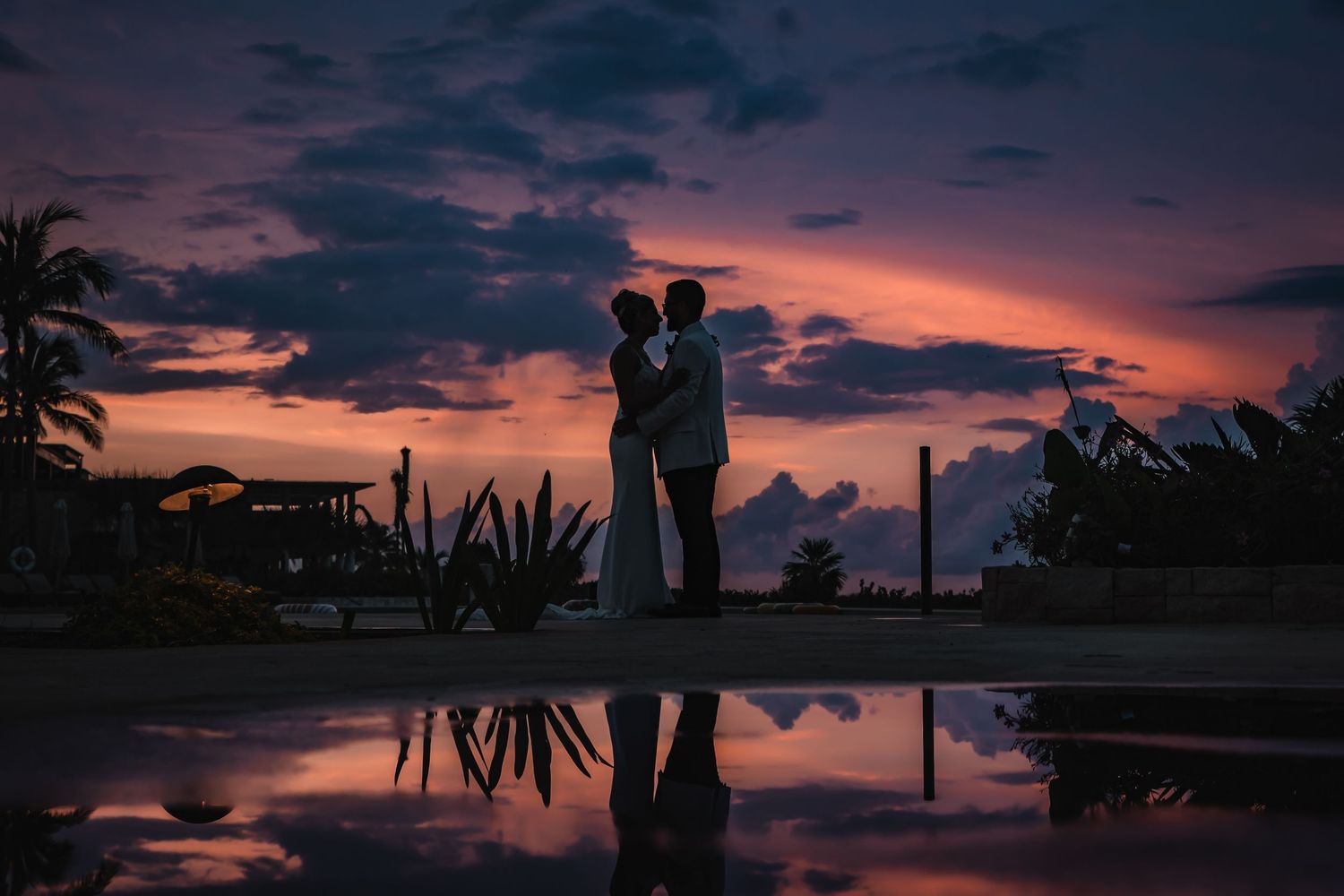 Silhouettes of wedding couple against vibrant orange tropical sunset.