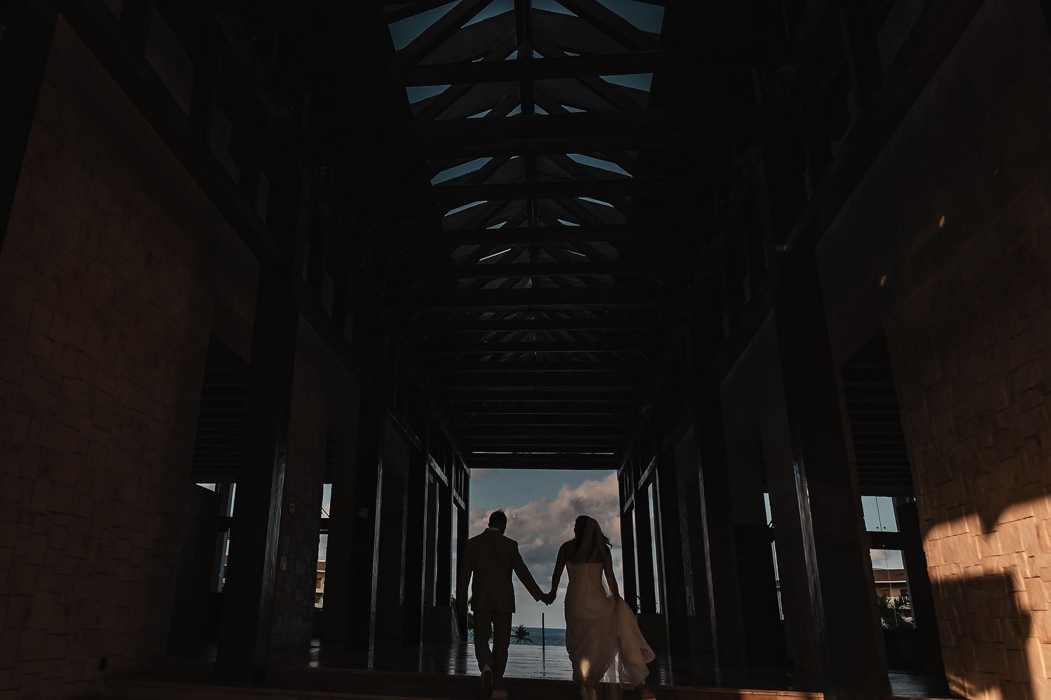 A dramatic silhouette of a couple holding hands in a dark hallway with natural light streaming in.