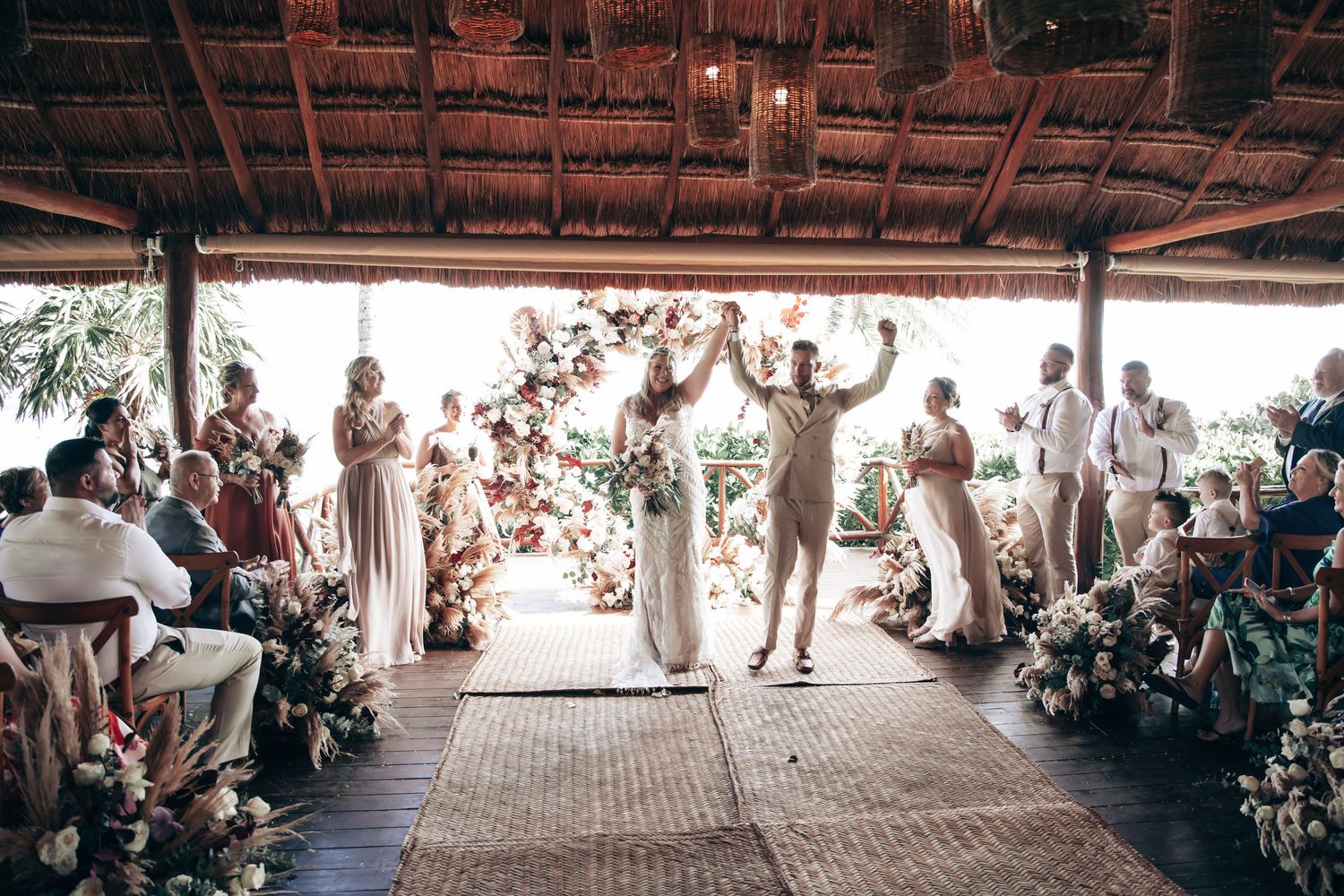 Bride and groom raising hands in celebration at the altar of a rustic open-air wedding venue.