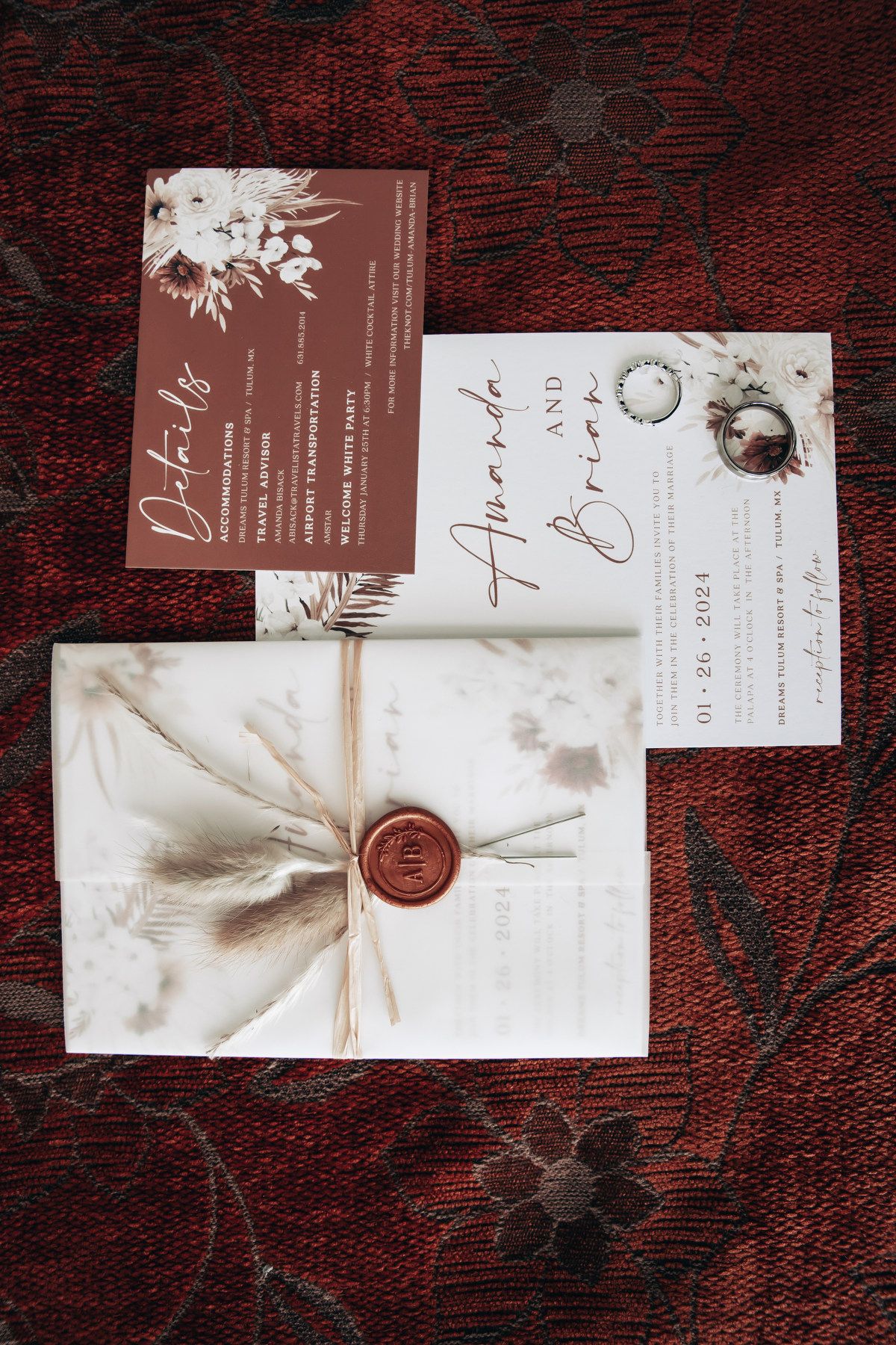 Boho wedding invitation suite with wax seal on a red floral fabric.