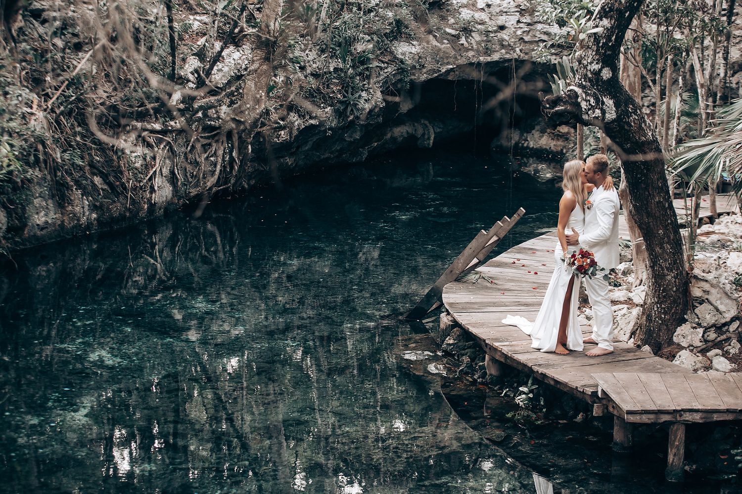 A couple embracing in a dreamy forest setting with natural light filtering through trees.