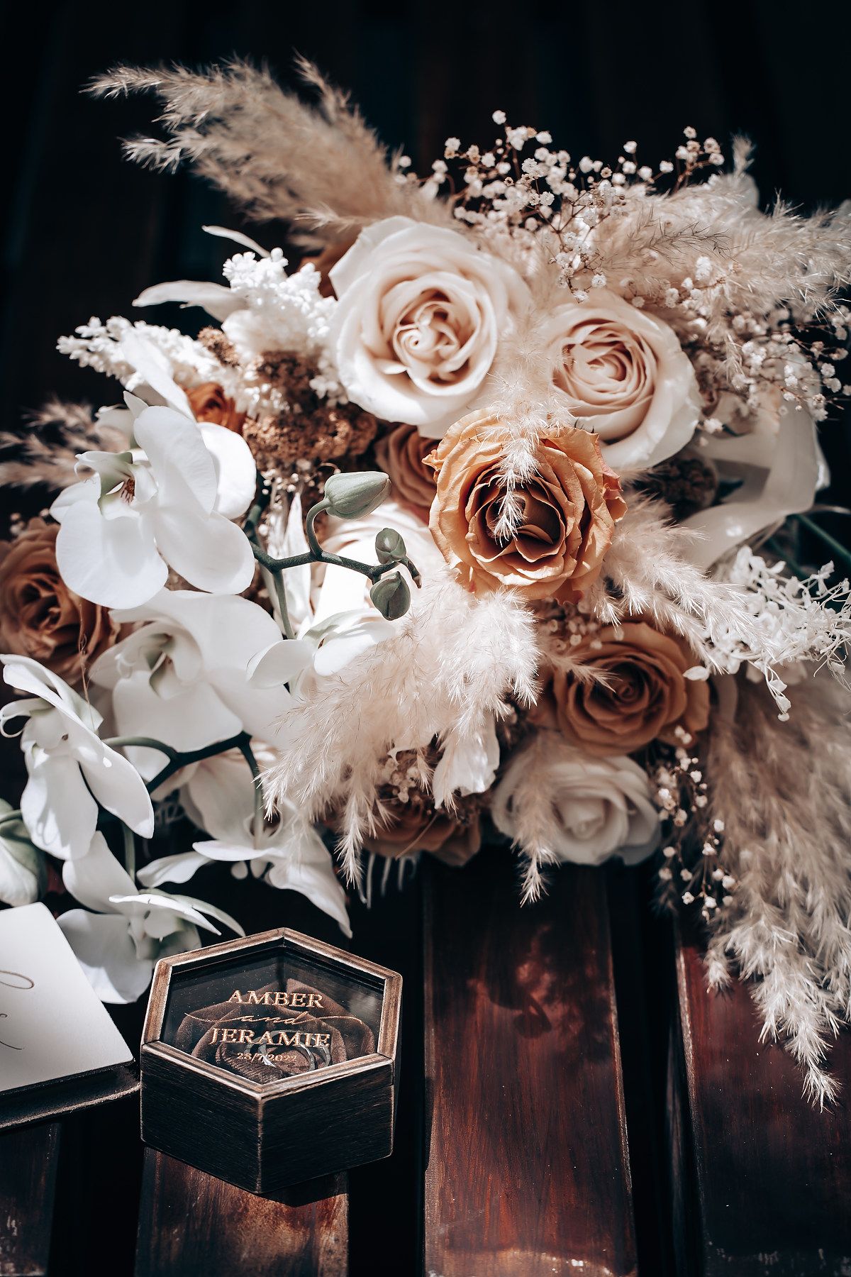 Elegant floral arrangement with blush roses, white orchids and pampas grass against dark wood with vintage hexagonal box.
