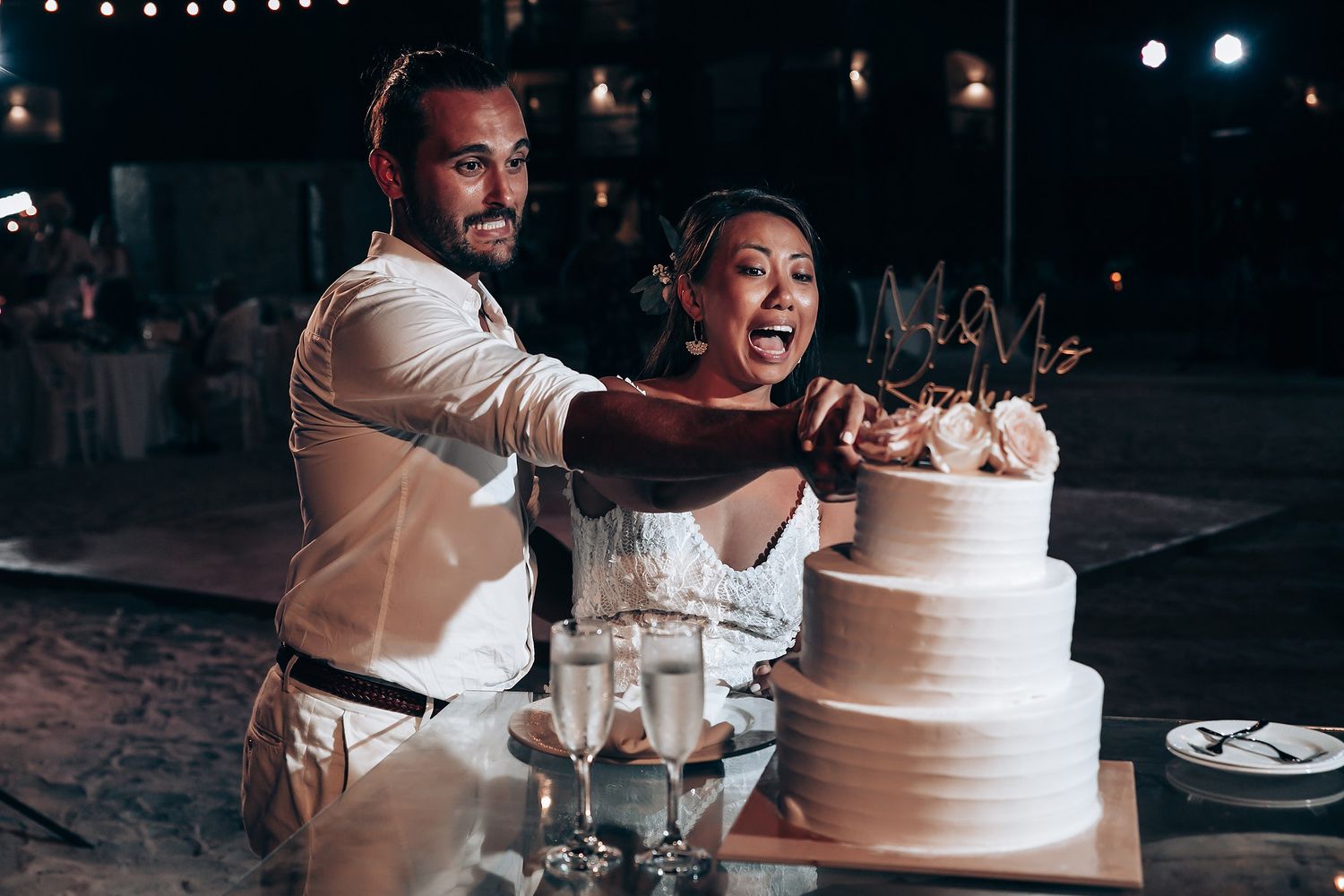 Wedding couple cuts their elegant white tiered cake together at the reception.