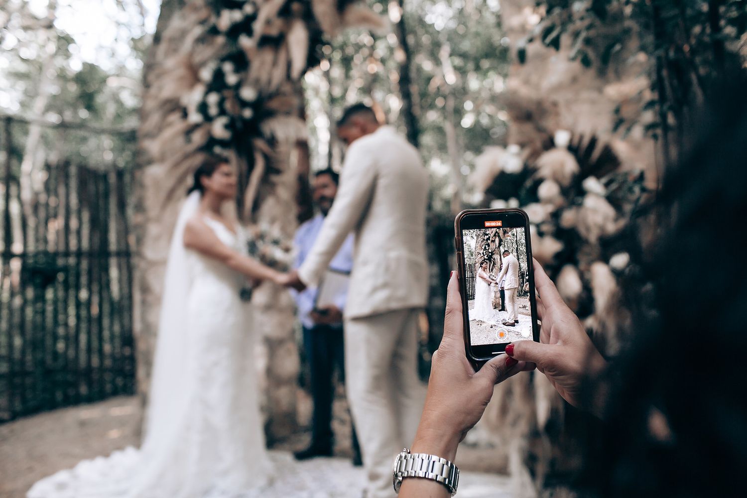 Wedding attendees capture photos on phones during an outdoor ceremony.