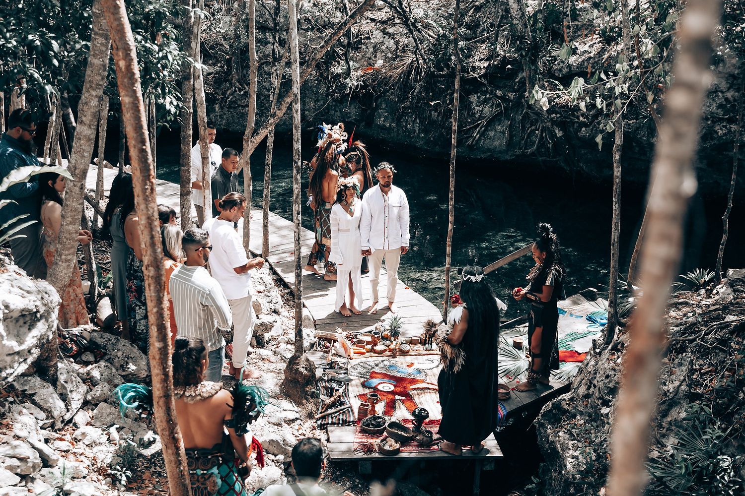Guests observe a traditional ceremony on an elevated wooden platform in a forest setting.