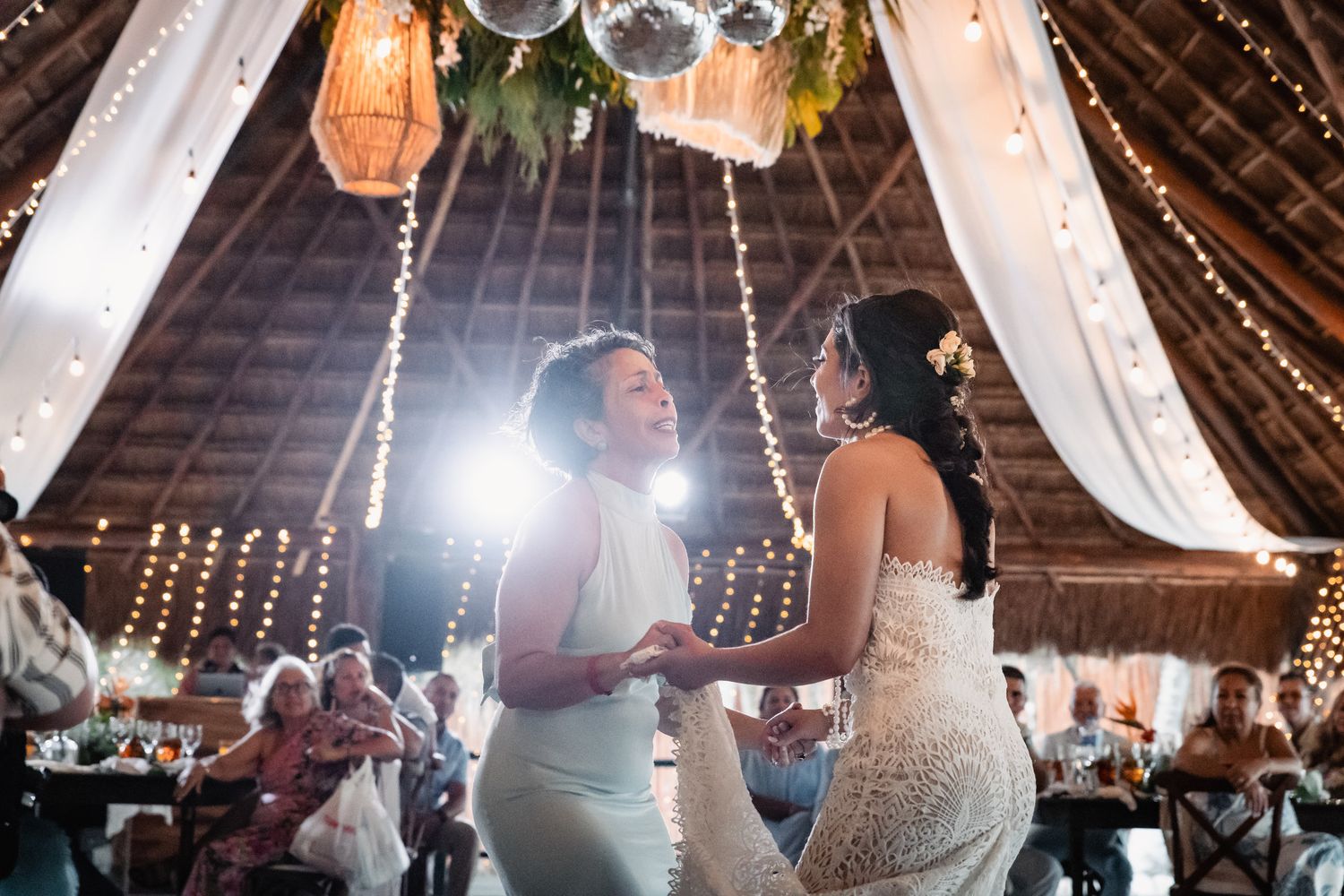 Two women sharing a joyful first dance under festive lights at reception.