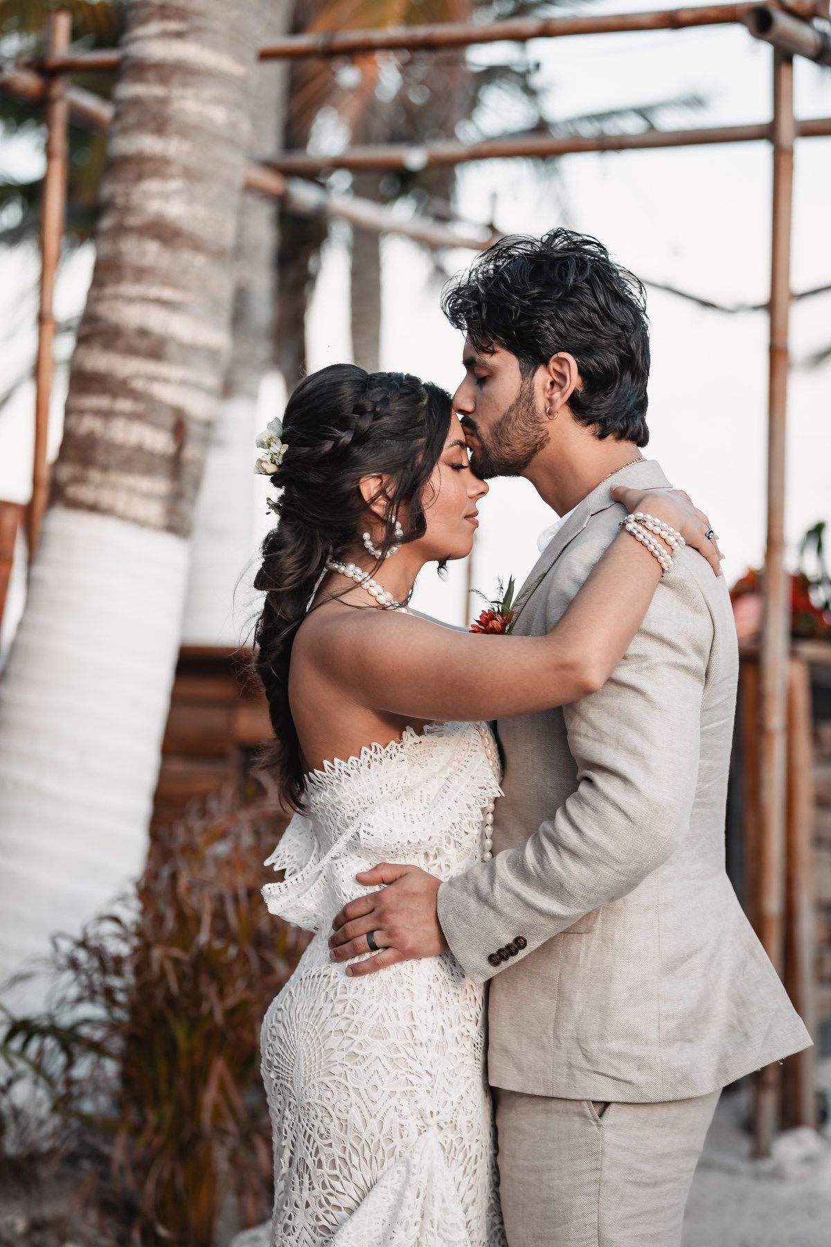 Bride and groom share intimate kiss during golden hour at tropical beach wedding venue.