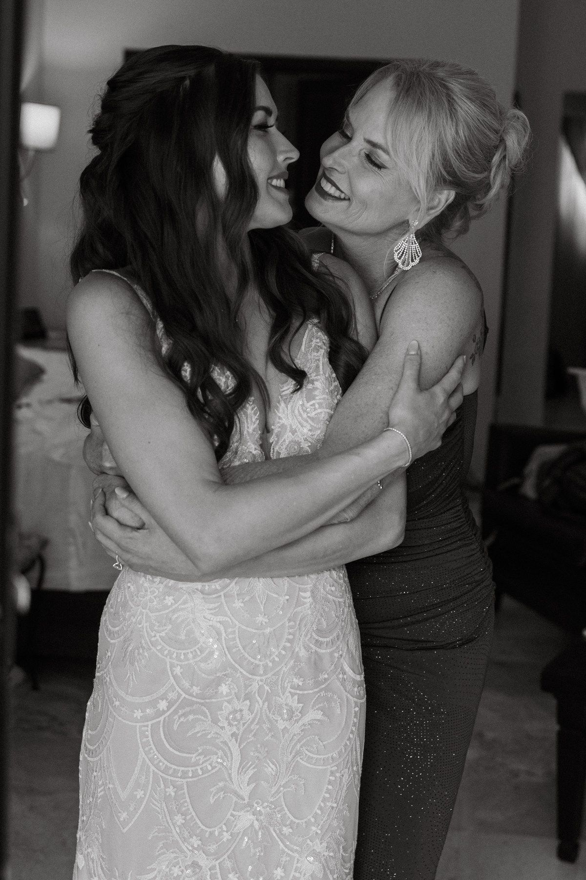 Bride and mother share a joyful embrace in black and white wedding photo.