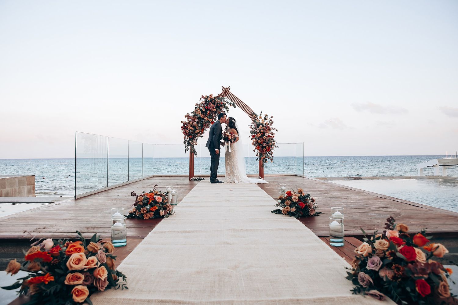 Wedding ceremony setup on an oceanfront pier with floral arch and pink flower arrangements.