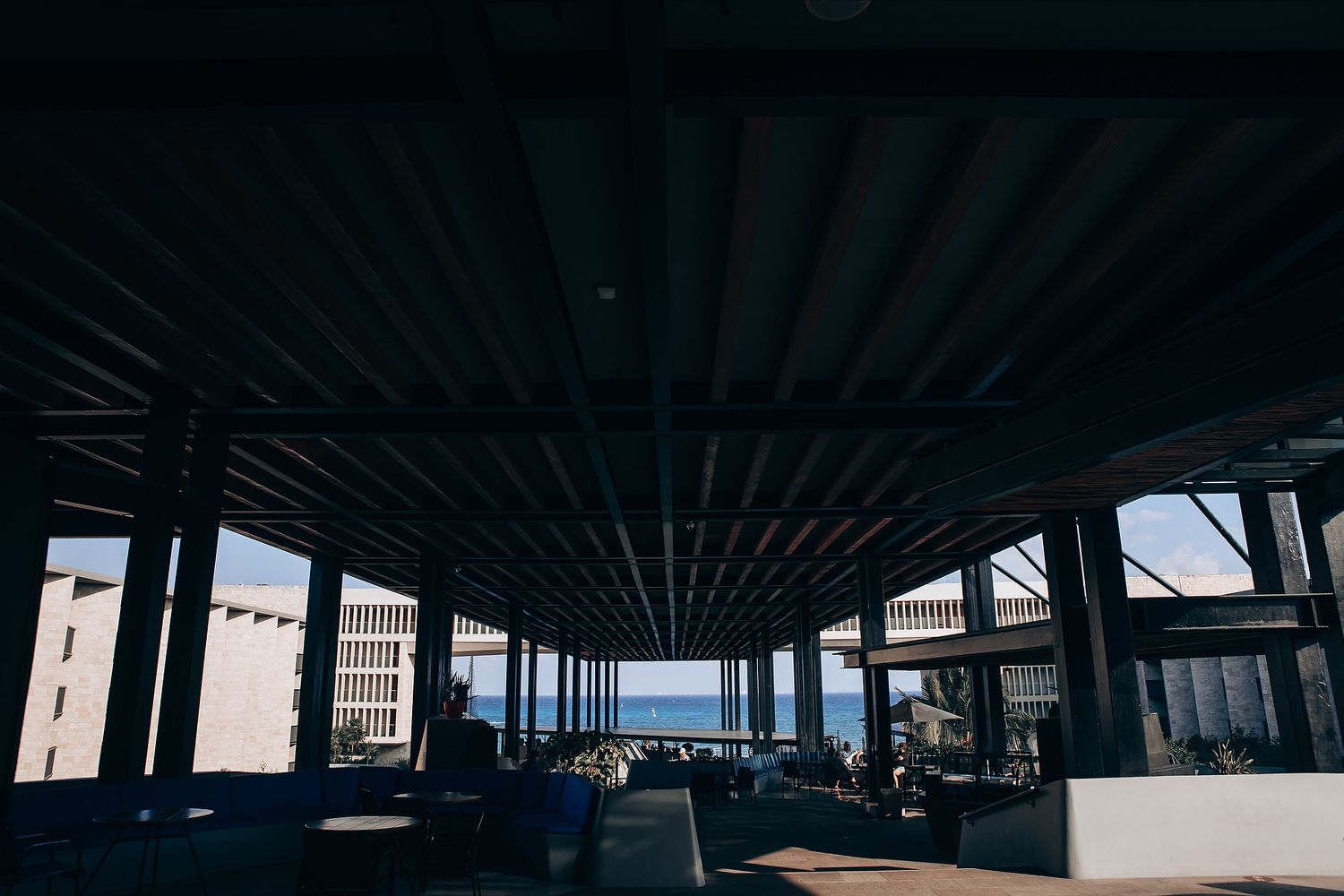A dark industrial interior space with repeating columns and beams stretches towards a bright window view at the end.