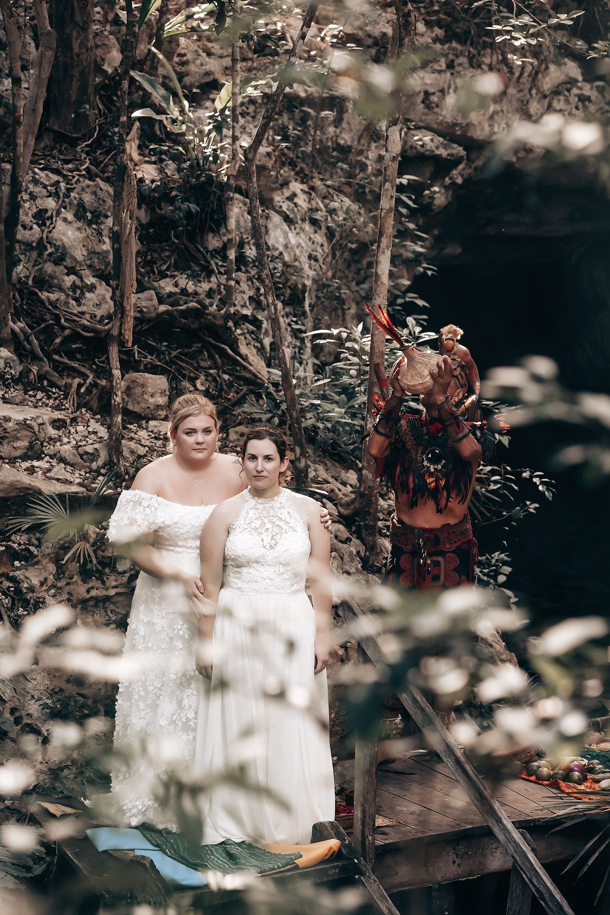 Two people in wedding attire standing in a lush, forested environment with a decorative arch and other elements.