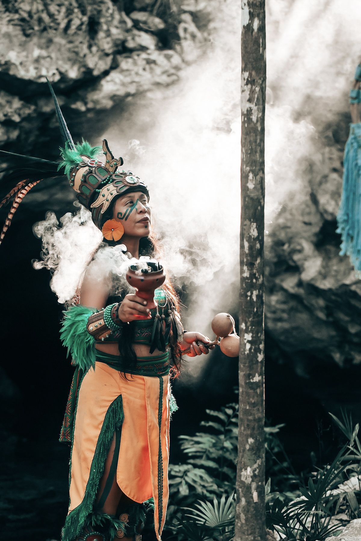 A person in traditional attire holds a ceremonial object and appears to be performing a ritual.