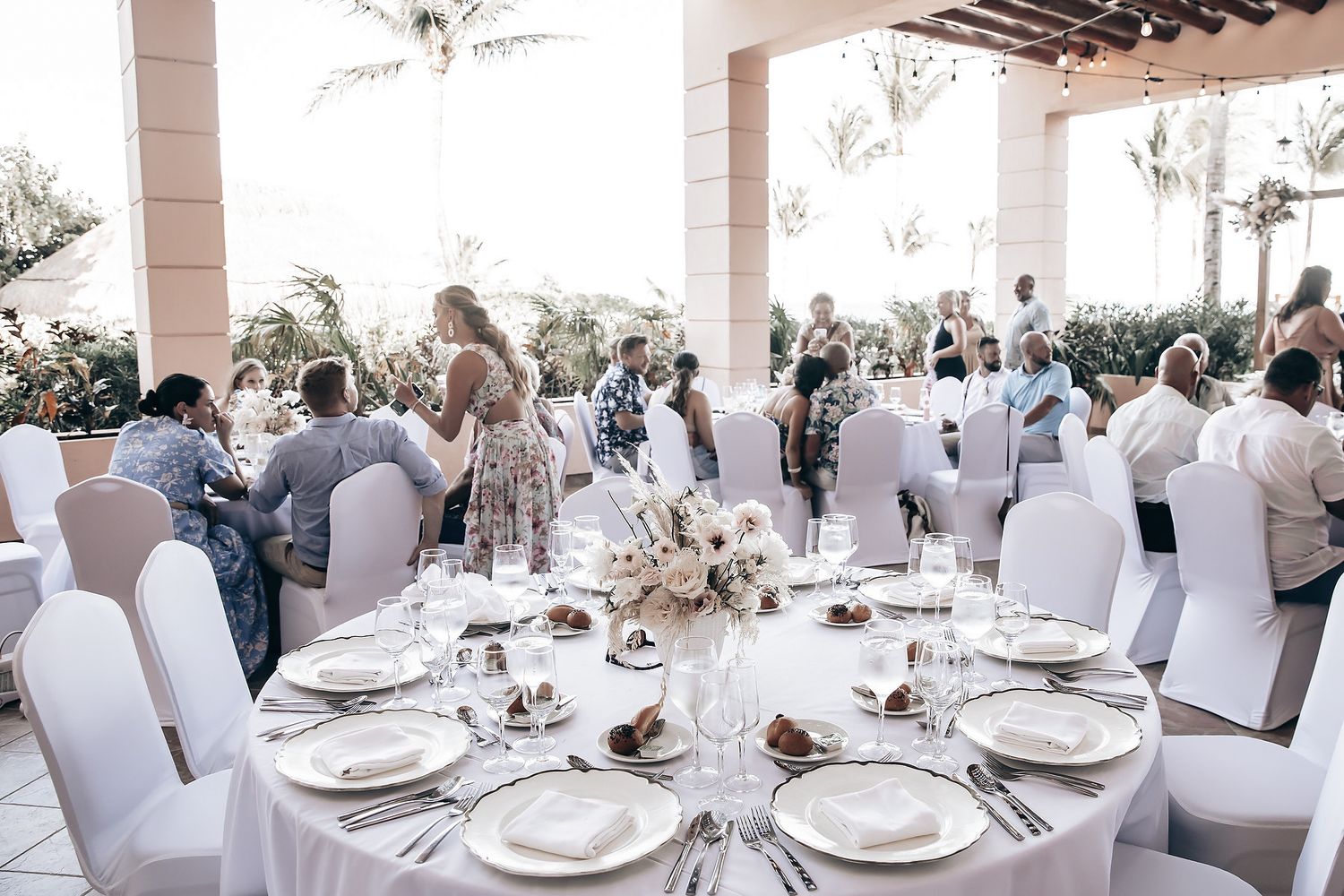 A large table is set for a formal wedding reception, with guests seated around it.