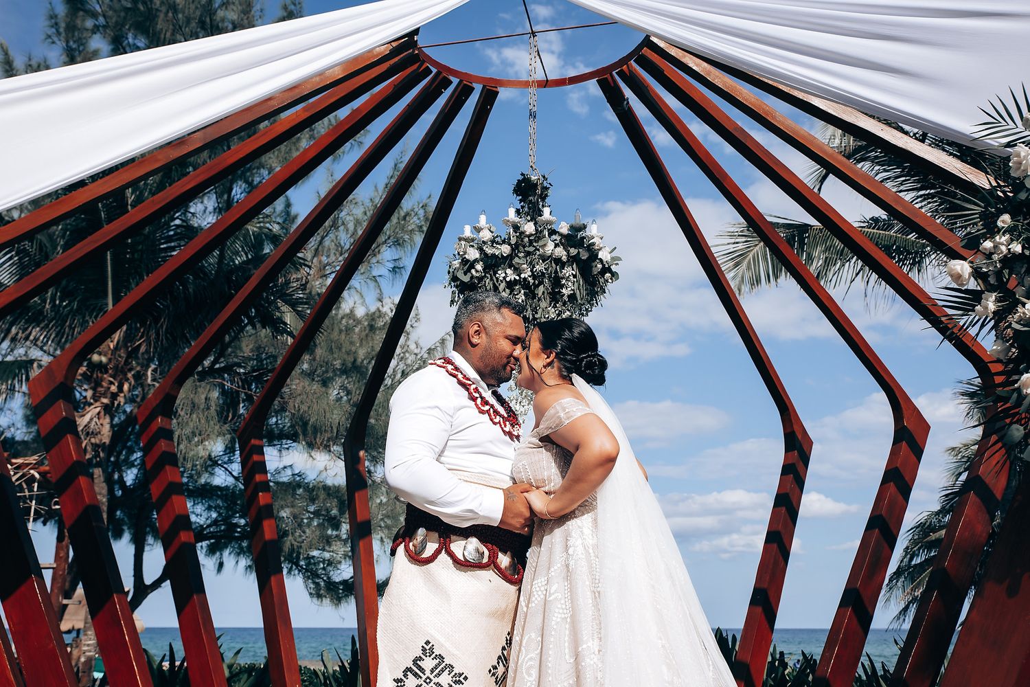 A wedding ceremony setup with white canopy and decorative red beams against a blue sky.