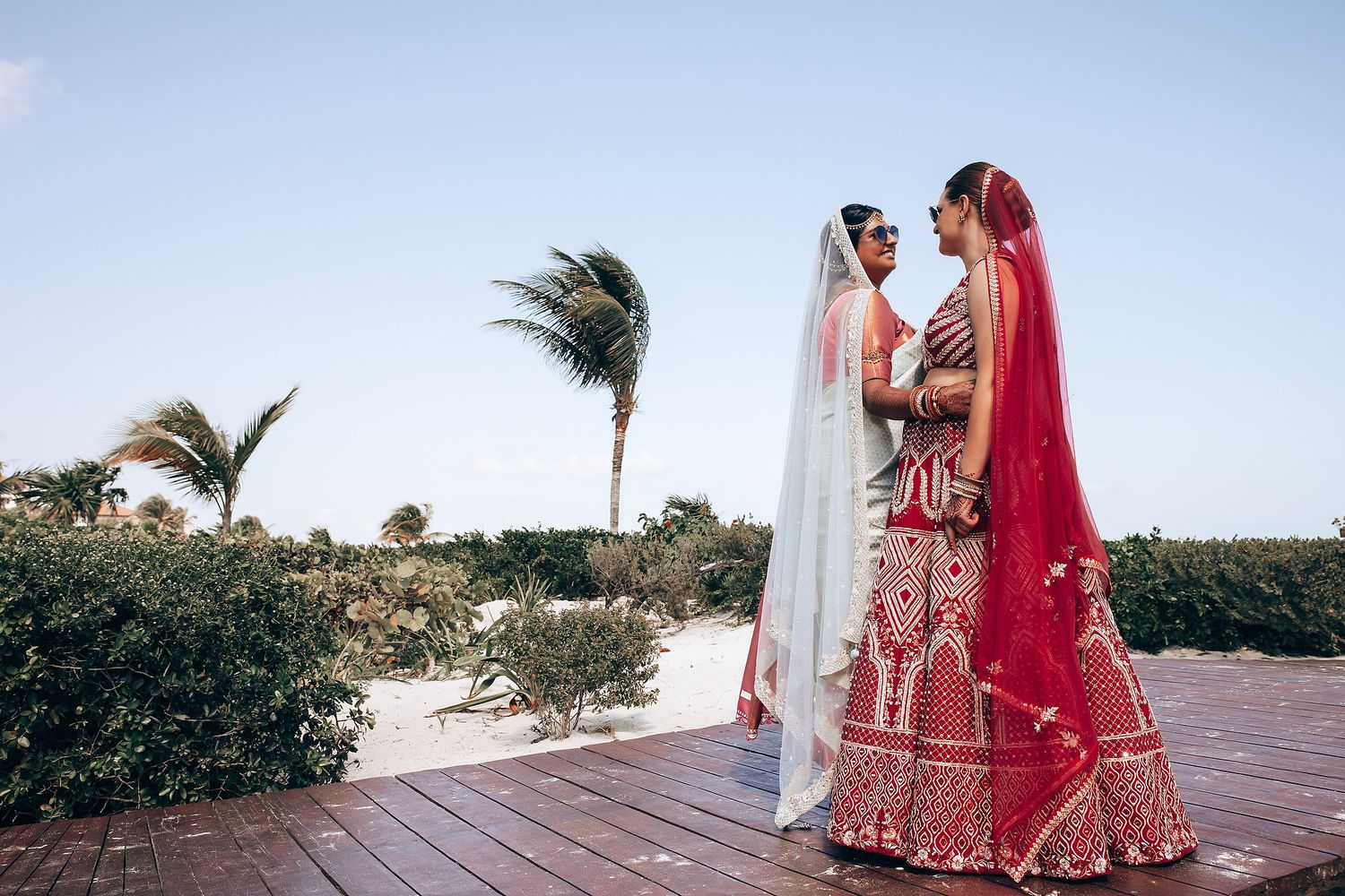 Traditional Indian wedding couple in red and white attire on outdoor deck.