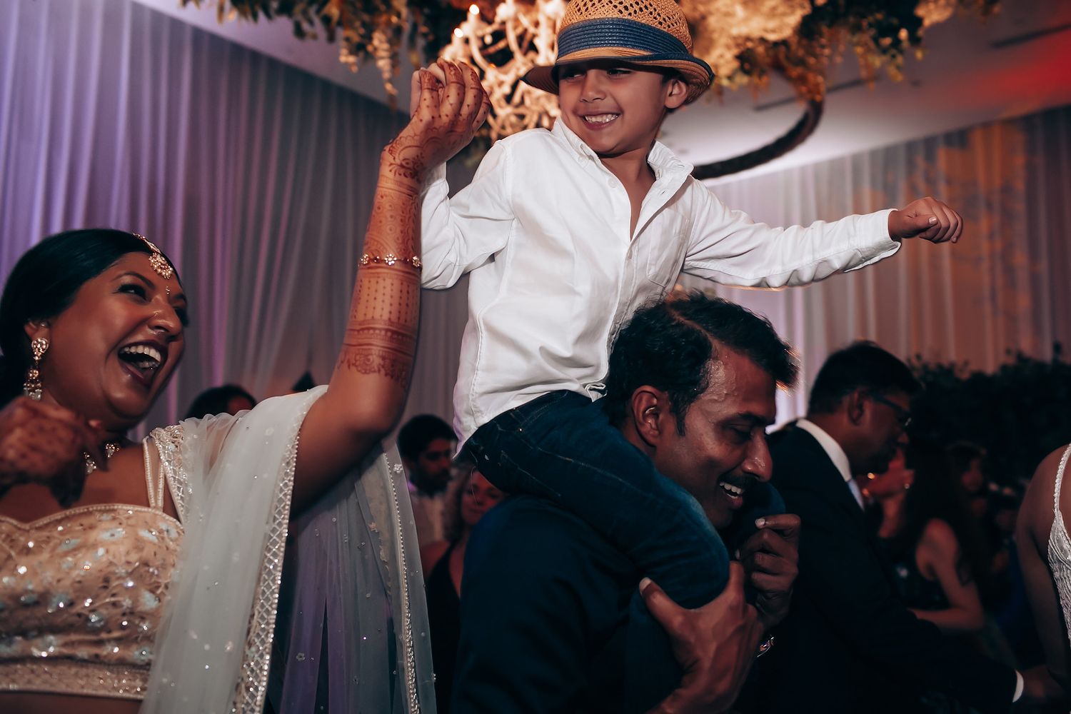 Wedding guests dancing and celebrating at a dimly lit reception with dramatic lighting.