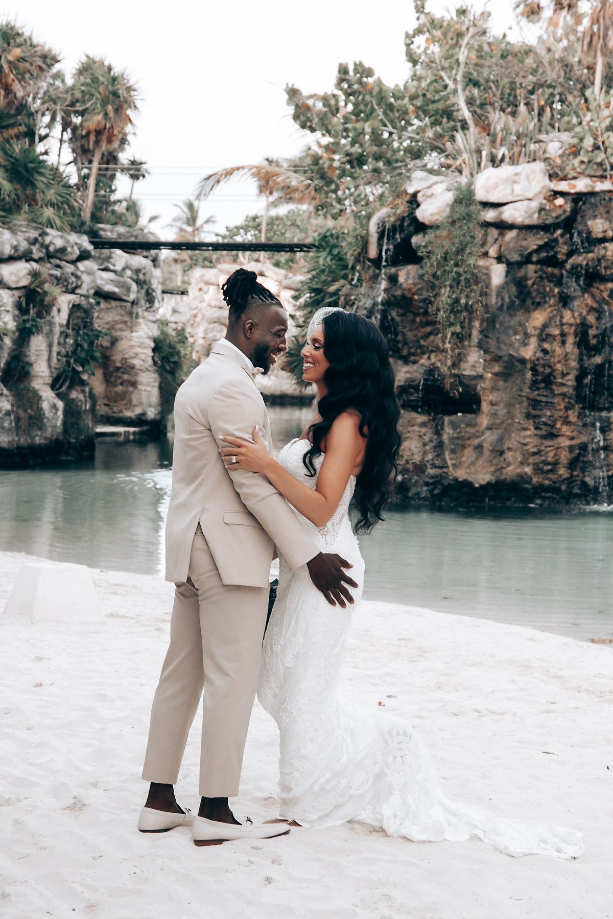 Wedding couple poses for romantic photos by a scenic waterfront with rock formations.