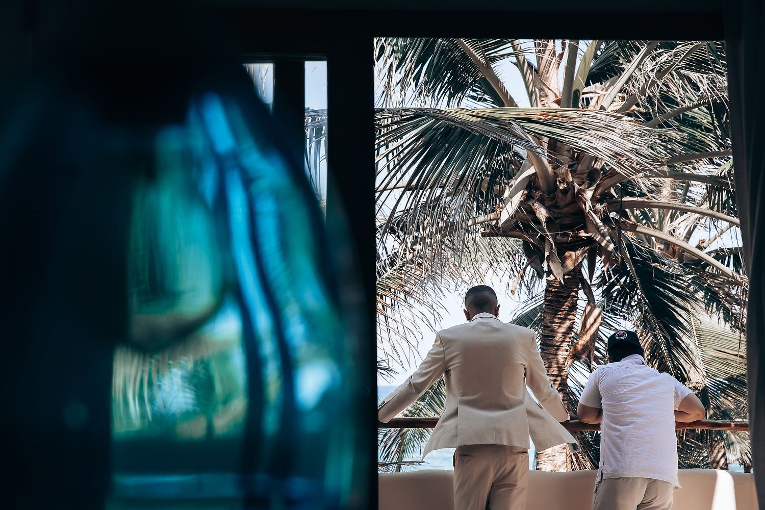 Silhouetted figures sitting on beach with palm trees and turquoise ocean views.
