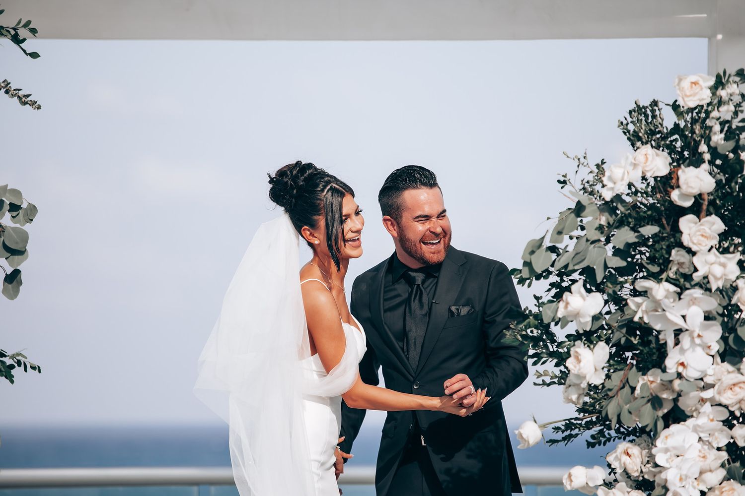 Outdoor wedding ceremony setup with white floral arrangements and ocean view.