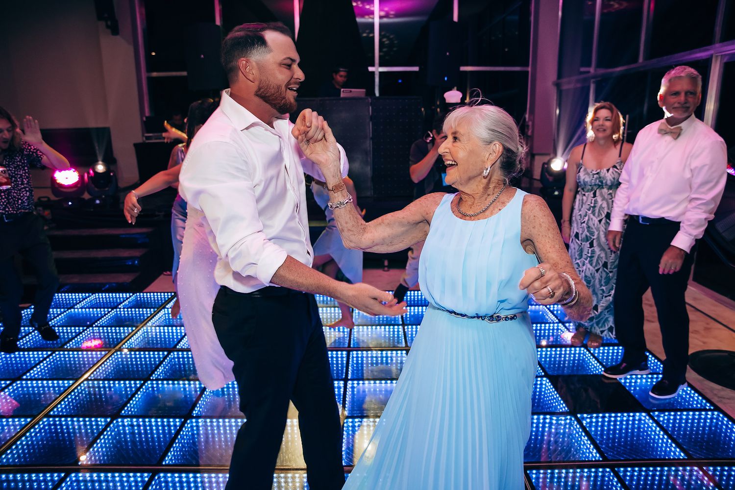 Guests dance on an illuminated blue LED dance floor at an elegant wedding reception.