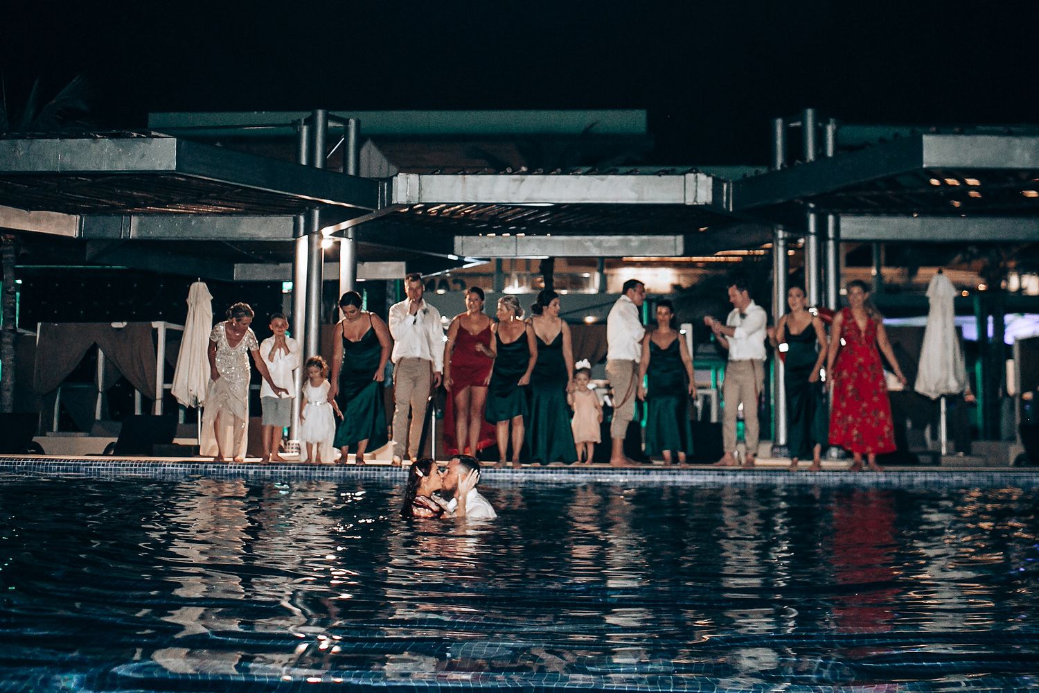 Wedding guests gathered around poolside venue during evening celebration.