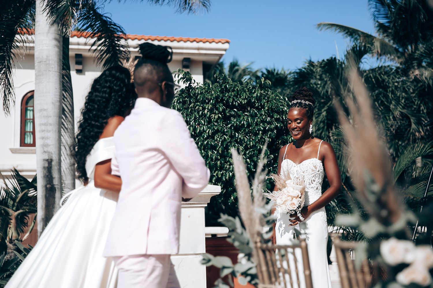 Wedding celebration group walking along a sunlit white stucco wall with tropical landscaping.