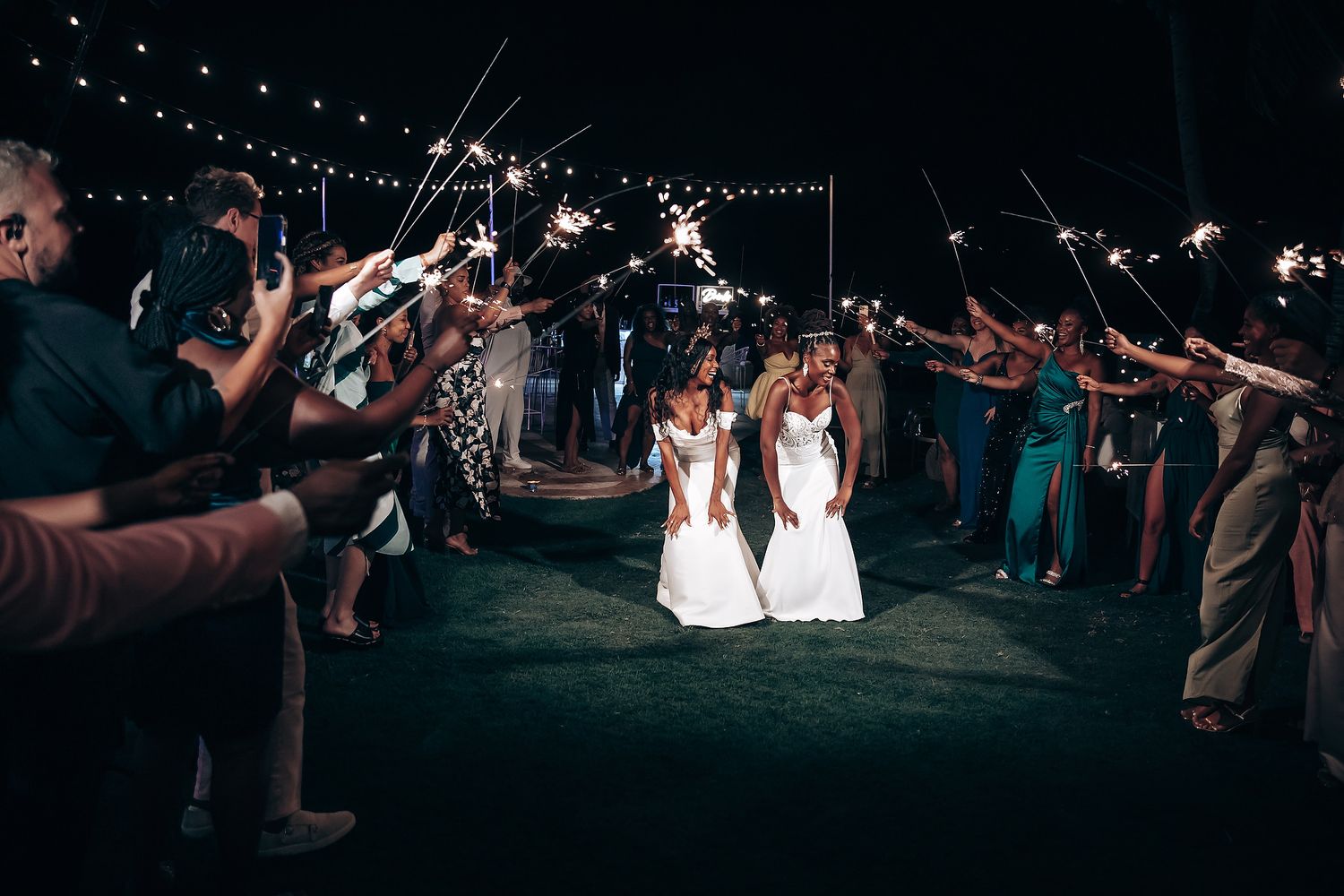 Evening outdoor wedding reception under string lights with guests celebrating.