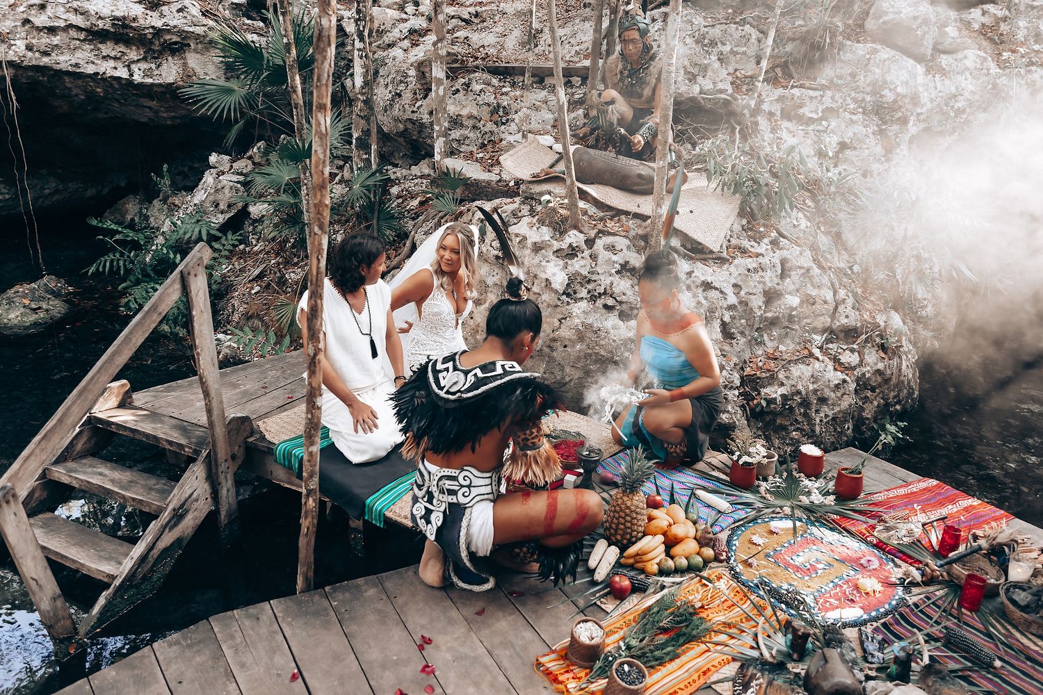 People gather around traditional cooking pots and fires in a rustic outdoor kitchen setting.