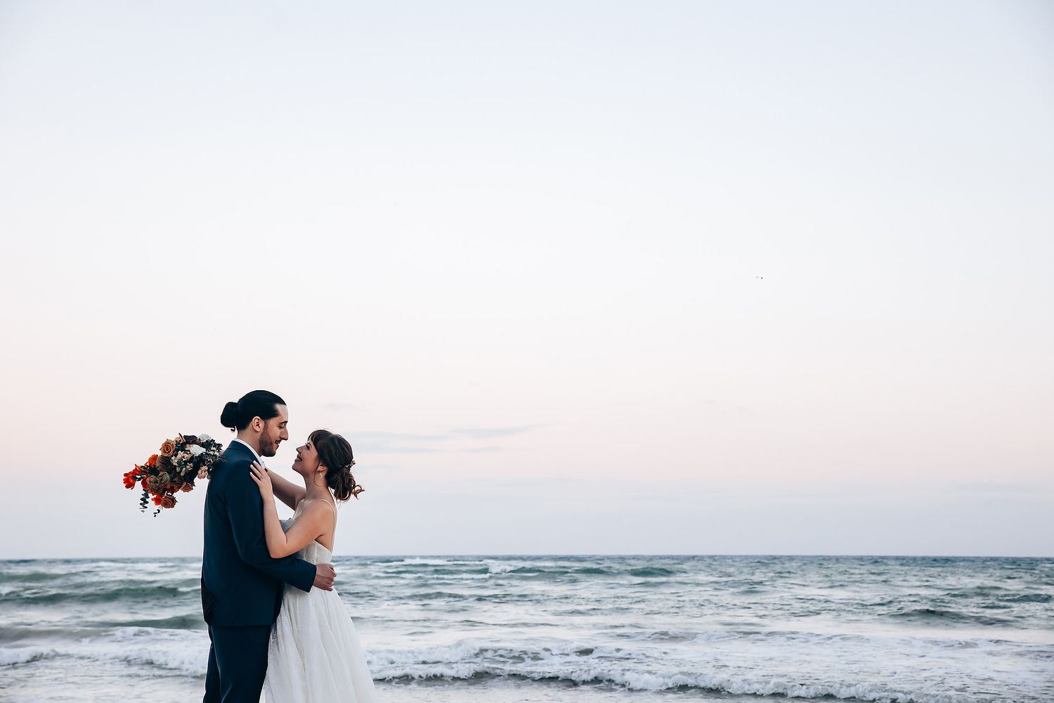 Romantic beachside wedding photos at sunset with waves crashing in the background.