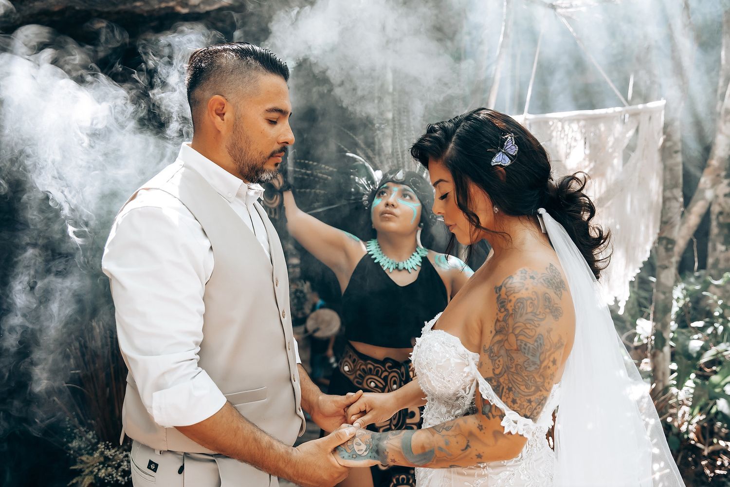 A couple exchanges rings during an outdoor wedding ceremony surrounded by atmospheric smoke in a forest setting.