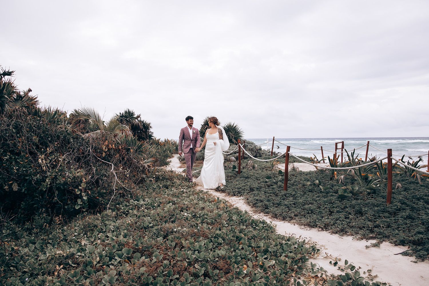 Wedding couple walking along a scenic coastal path surrounded by tropical vegetation.