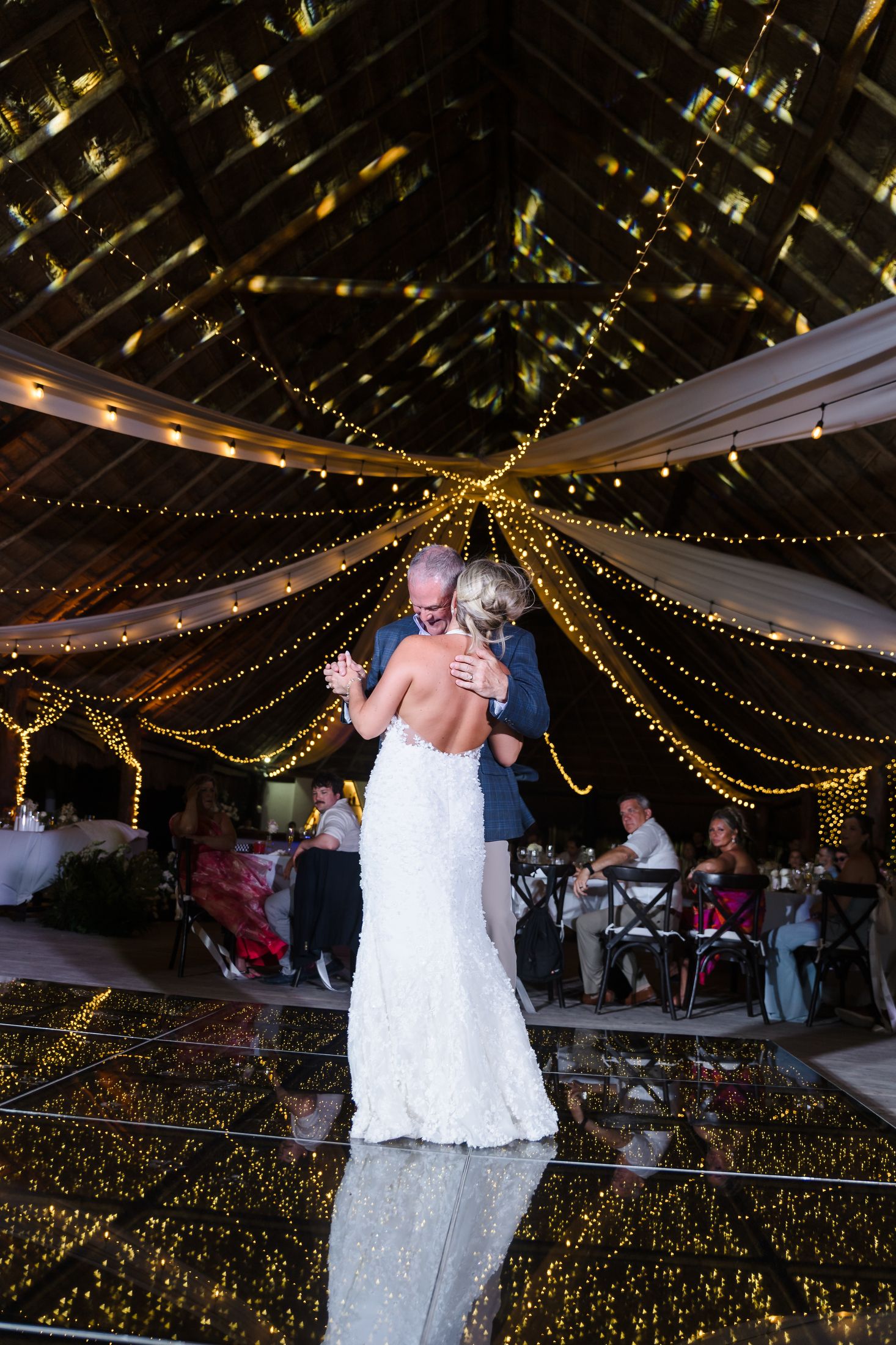 Bride and groom share first dance under fairy lights and draped ceiling at romantic wedding reception.