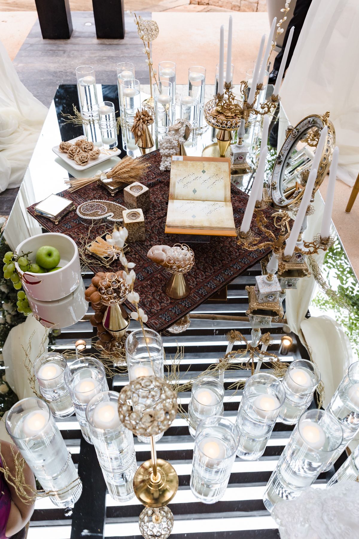 Elegant Persian wedding sofreh aghd table with candles, gold accents, mirror, and traditional ceremonial items on ornate rug.