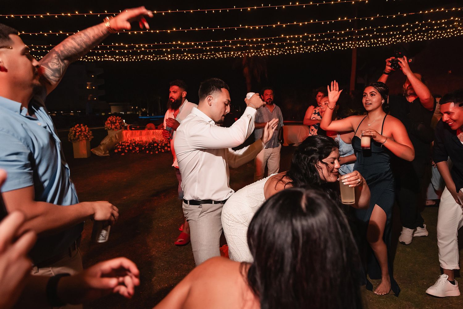Guests dancing energetically at an outdoor wedding reception under string lights at night.