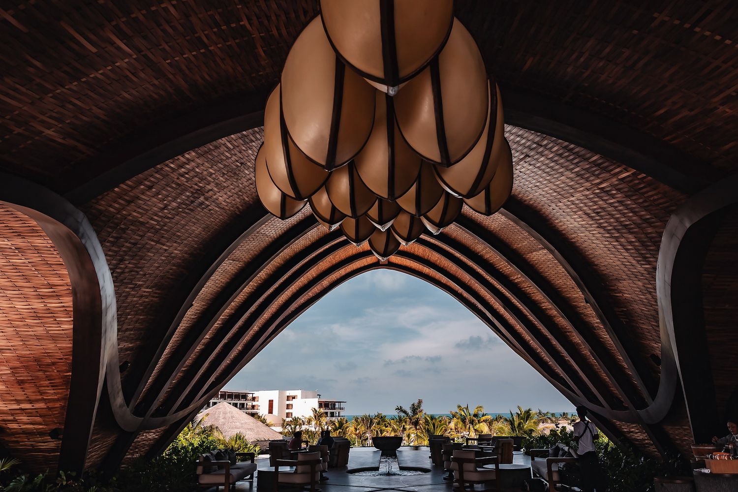 Stunning open-air resort pavilion with arched bamboo ceiling and ornate pendant light framing a tropical garden view.