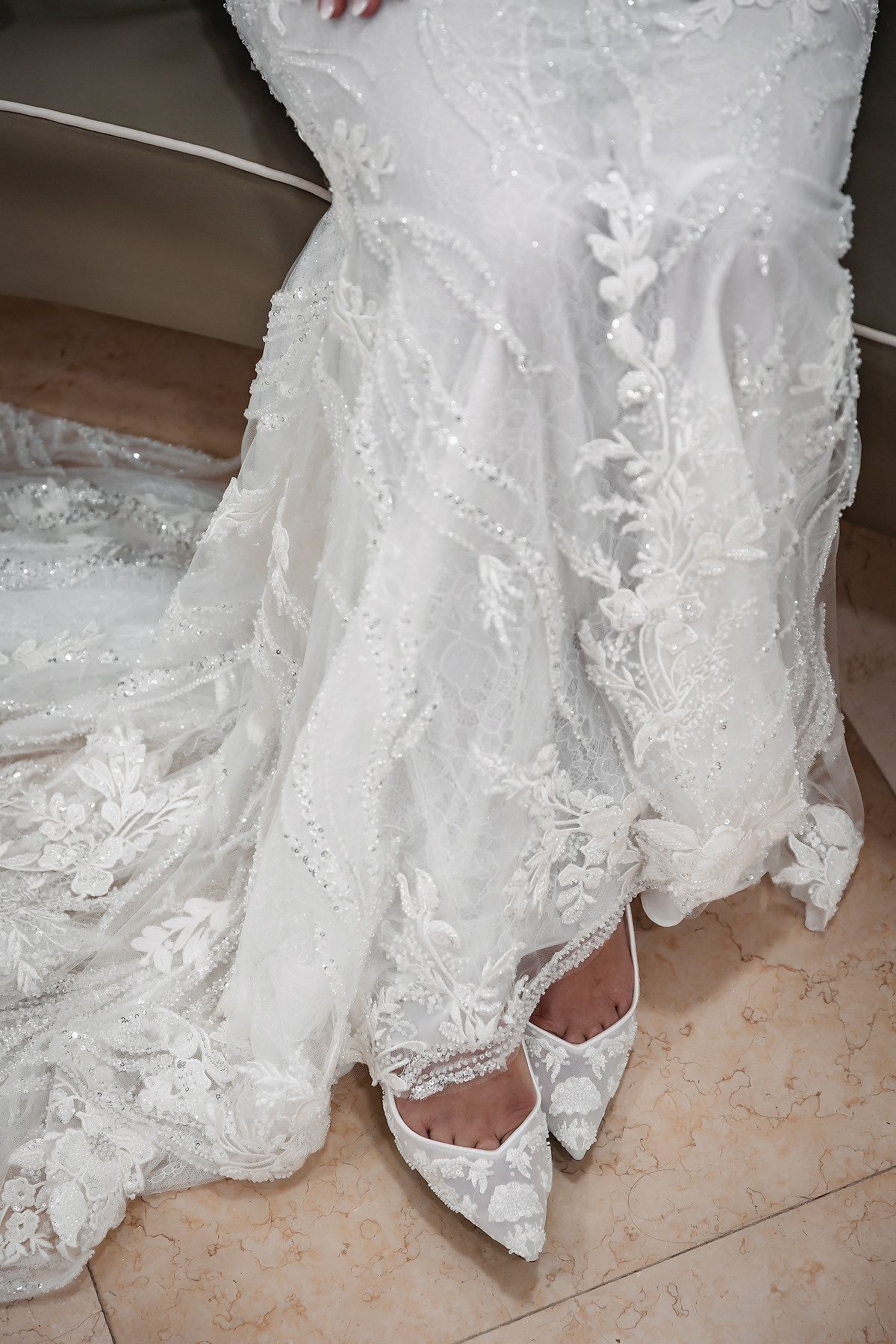 Elegant white lace wedding dress with floral embroidery and matching lace bridal heels on marble floor.