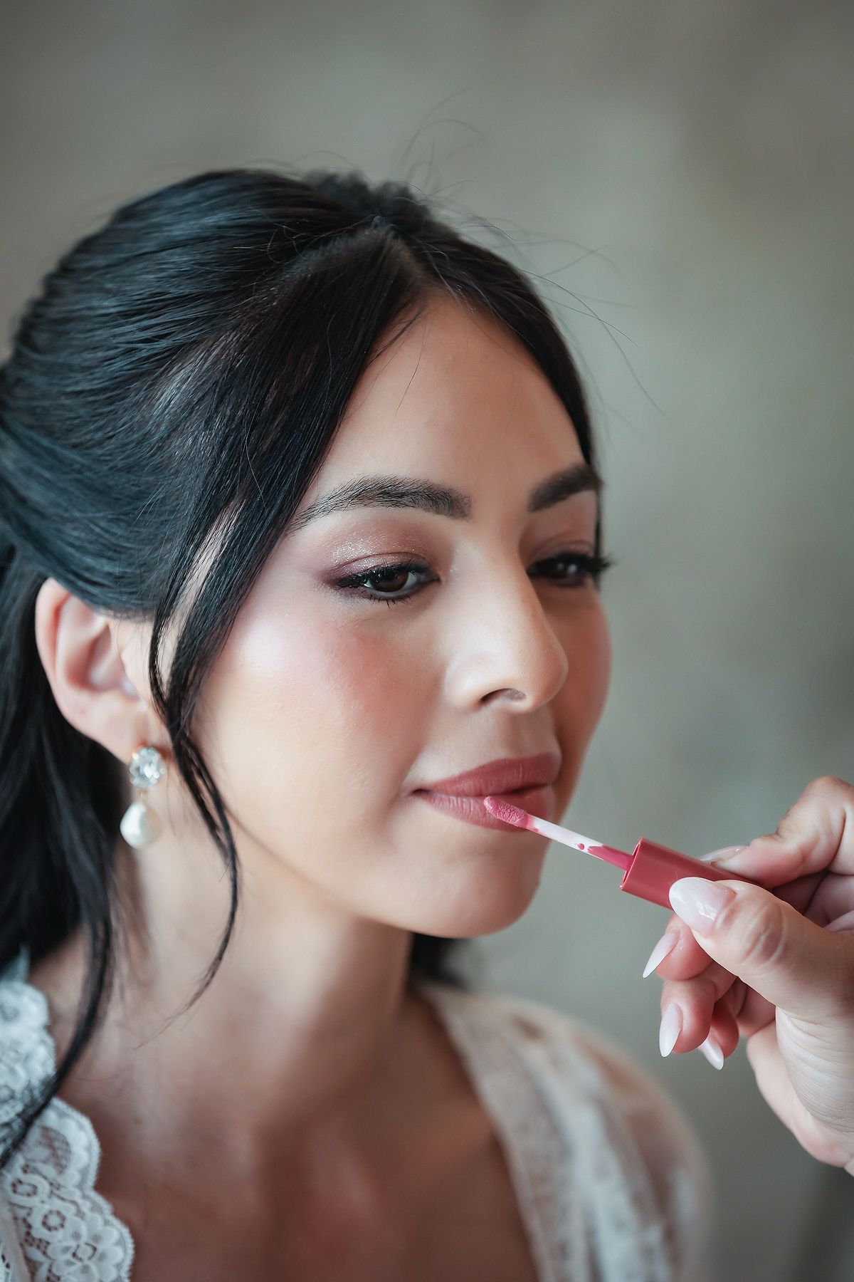 Bride getting pink lip gloss applied by makeup artist on her wedding day.