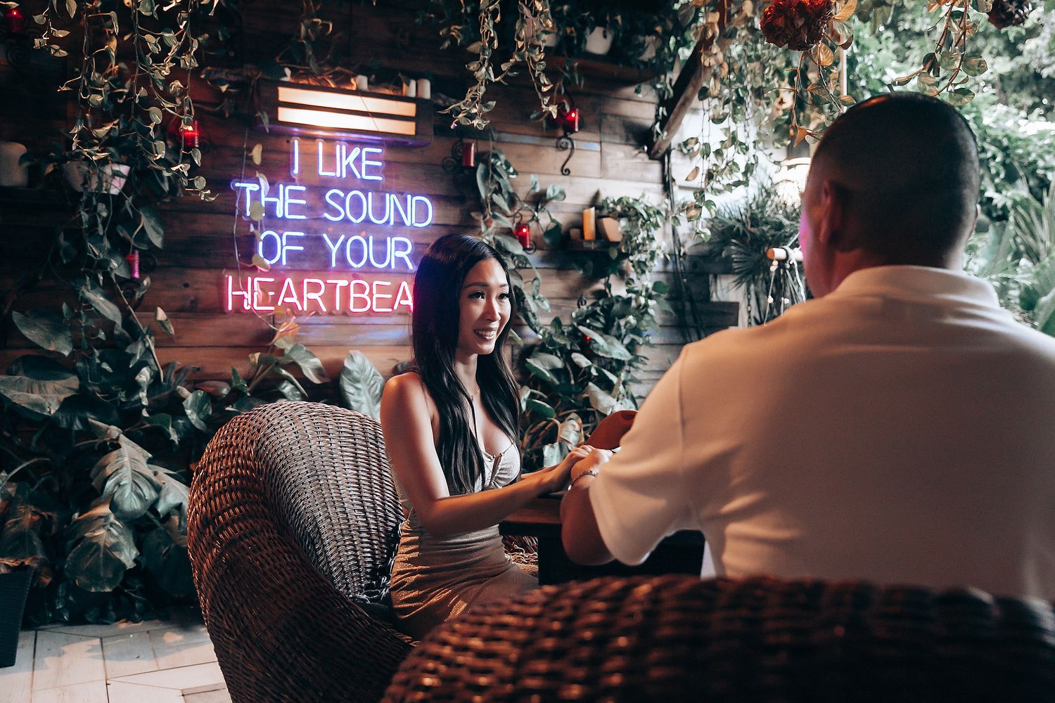 Couple on a romantic date in a cozy decorated venue with a neon sign reading I Like The Sound Of Your Heartbeat.
