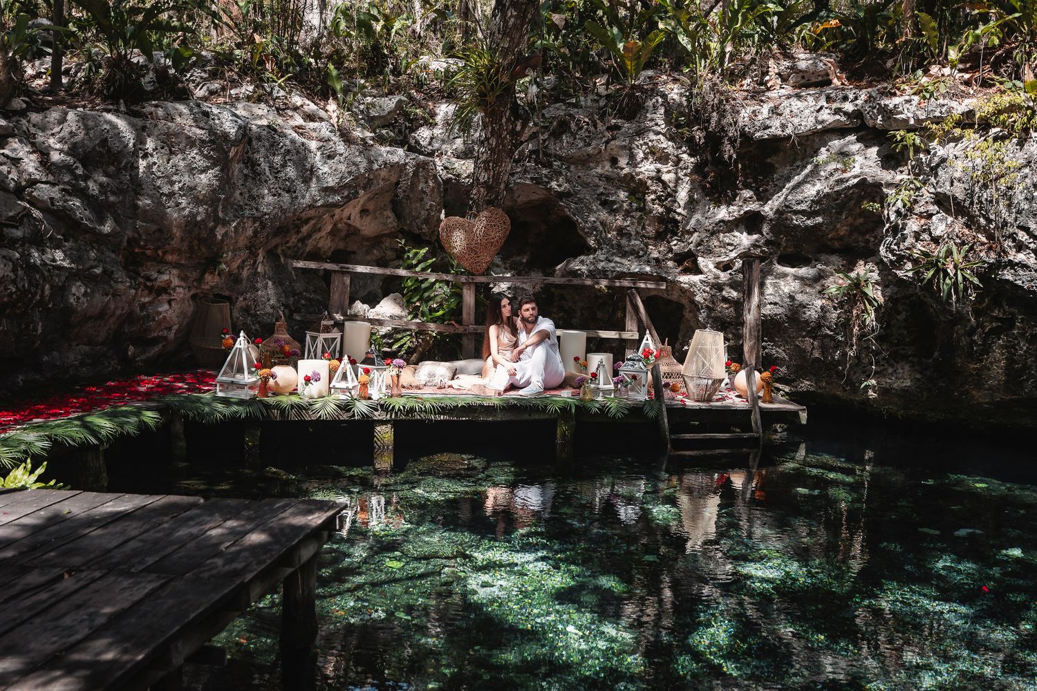 Couple relaxing on a wooden platform over a crystal-clear cenote surrounded by lush jungle rocks in Mexico.
