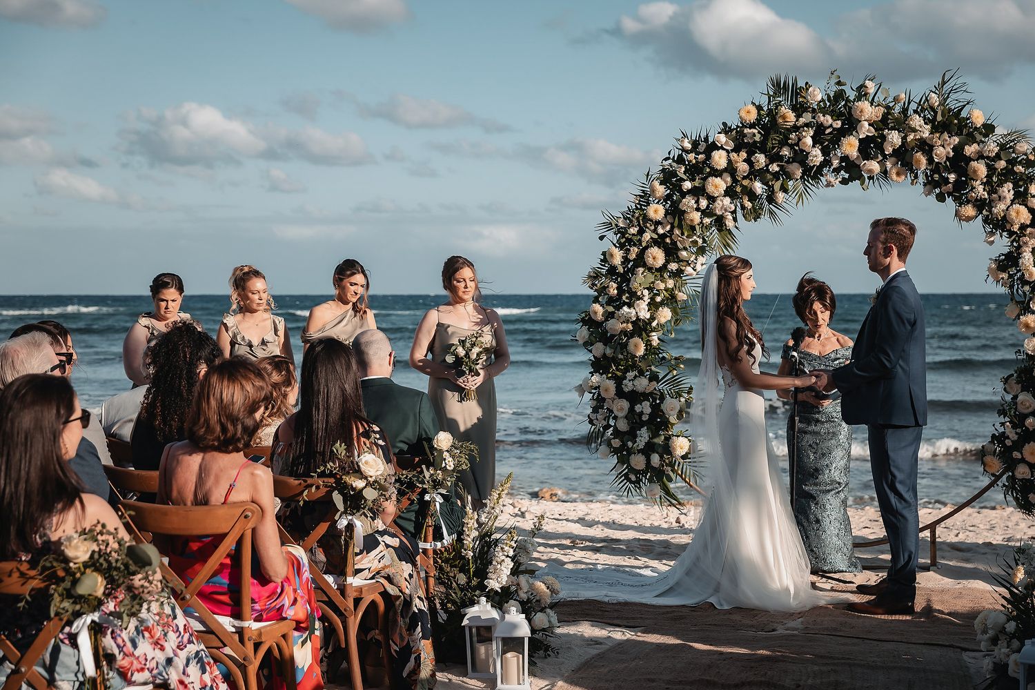 Romantic beach wedding ceremony with floral arch, bride and groom exchanging vows by the ocean.