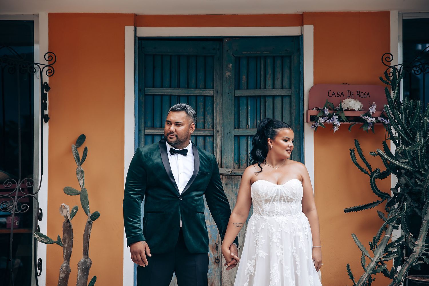 Wedding party walking along an orange-colored building exterior with dark wooden doors.